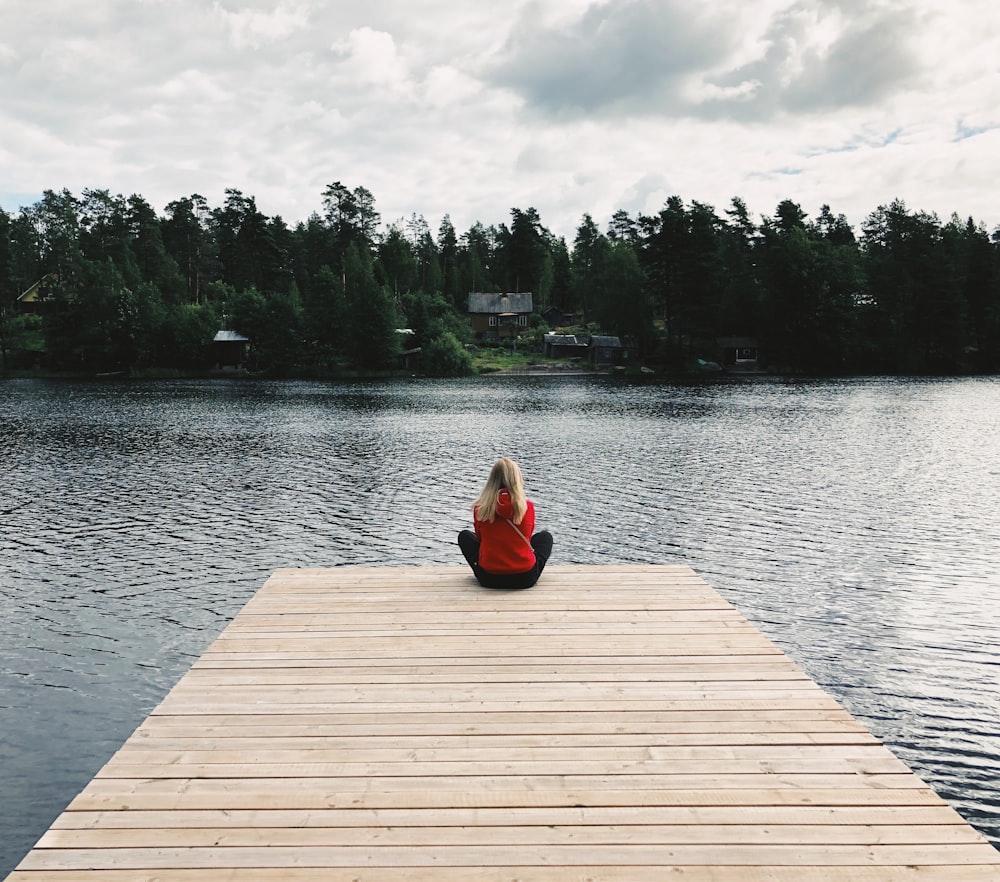 Femme assise sur un quai en bois sous des nuages blancs