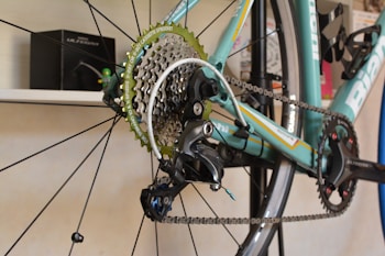 Close-up of the rear gear cassette and derailleur of a bicycle, showcasing intricate components and chain link details. The bicycle features a light blue frame with branding and the words Shimano and Ultegra visible on the components.
