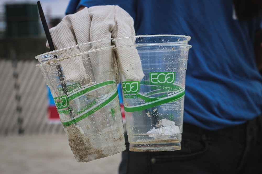 透明なプラスチック製の使い捨てカップを2つ持っている人