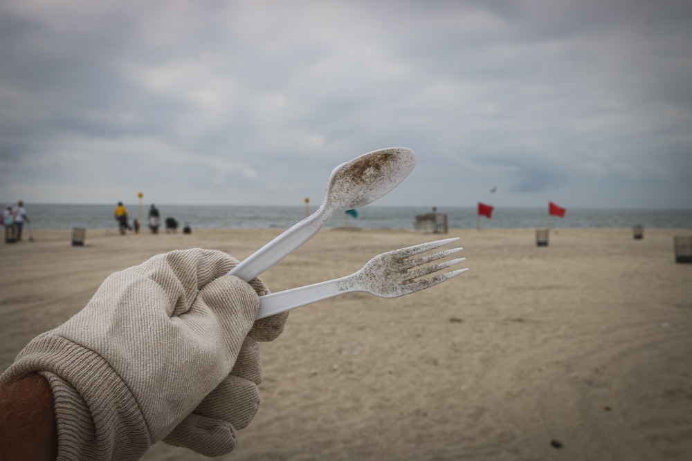 personne tenant une fourchette et une cuillère jetables en plastique blanc