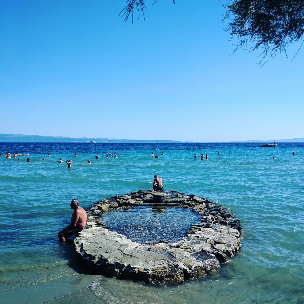 man sitting on rocky under clear blue sky