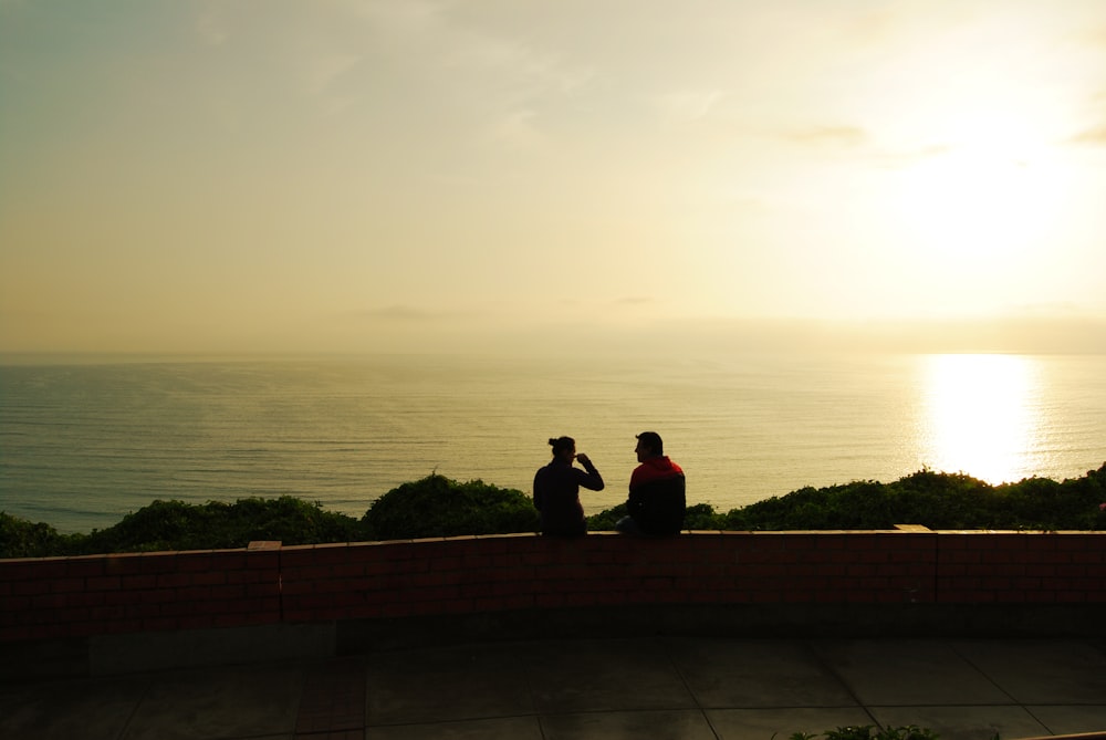 man and woman sitting on railing at sunrise