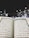 An open Quran is prominently displayed, with Arabic text visible on both pages. The background features an outdoor setting at night, with the Kaaba surrounded by worshippers wearing white clothing, indicative of a religious gathering.