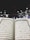 An open Quran is prominently displayed, with Arabic text visible on both pages. The background features an outdoor setting at night, with the Kaaba surrounded by worshippers wearing white clothing, indicative of a religious gathering.