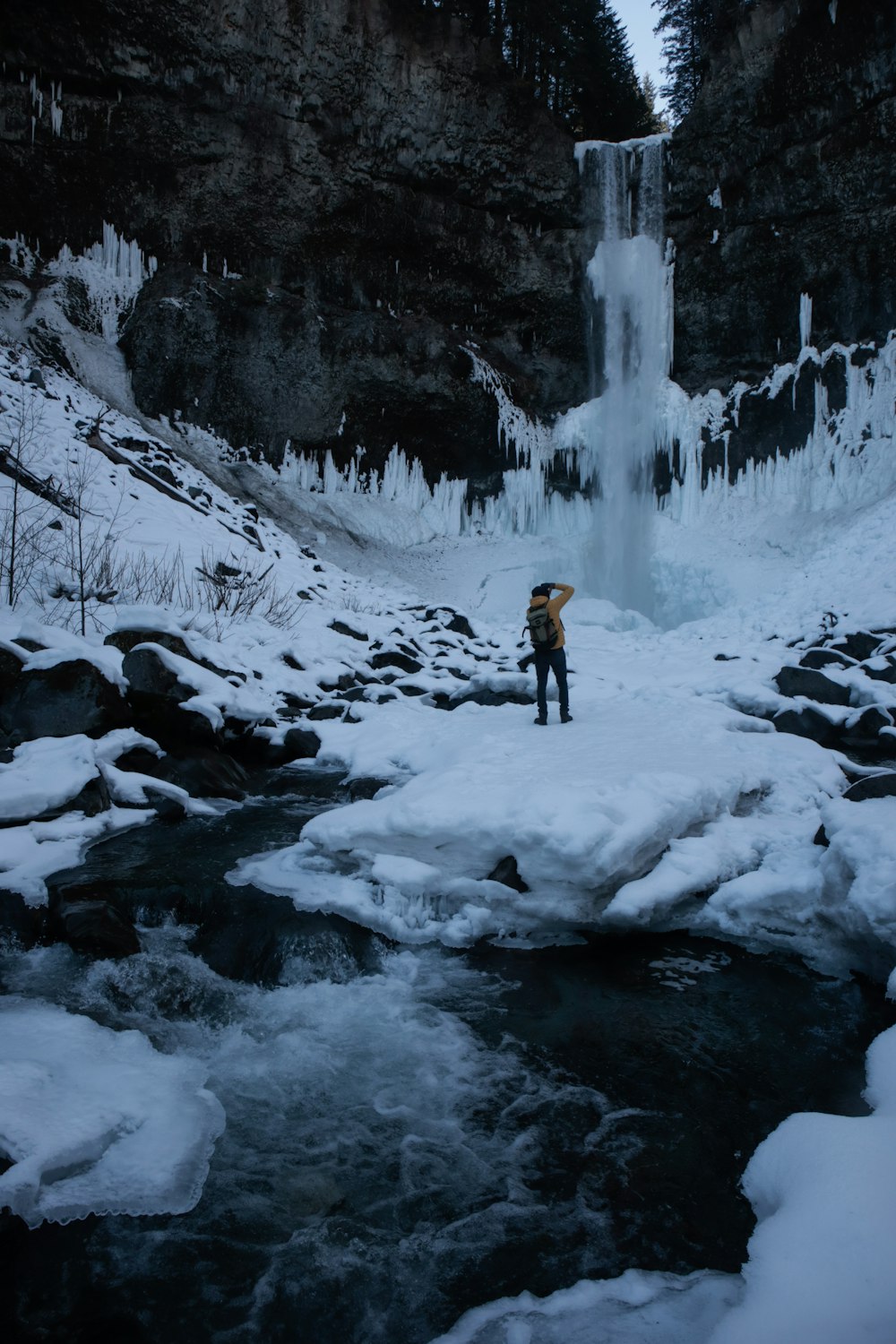 man standing on snow covered rock near waterfall