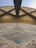 An architectural detail featuring a large, geometric pattern on a wall with intricate tile work. The tiles are decorated with blue, green, and brown colors, forming symmetrical designs. Above, there is a significant overhang, likely part of a roof structure.