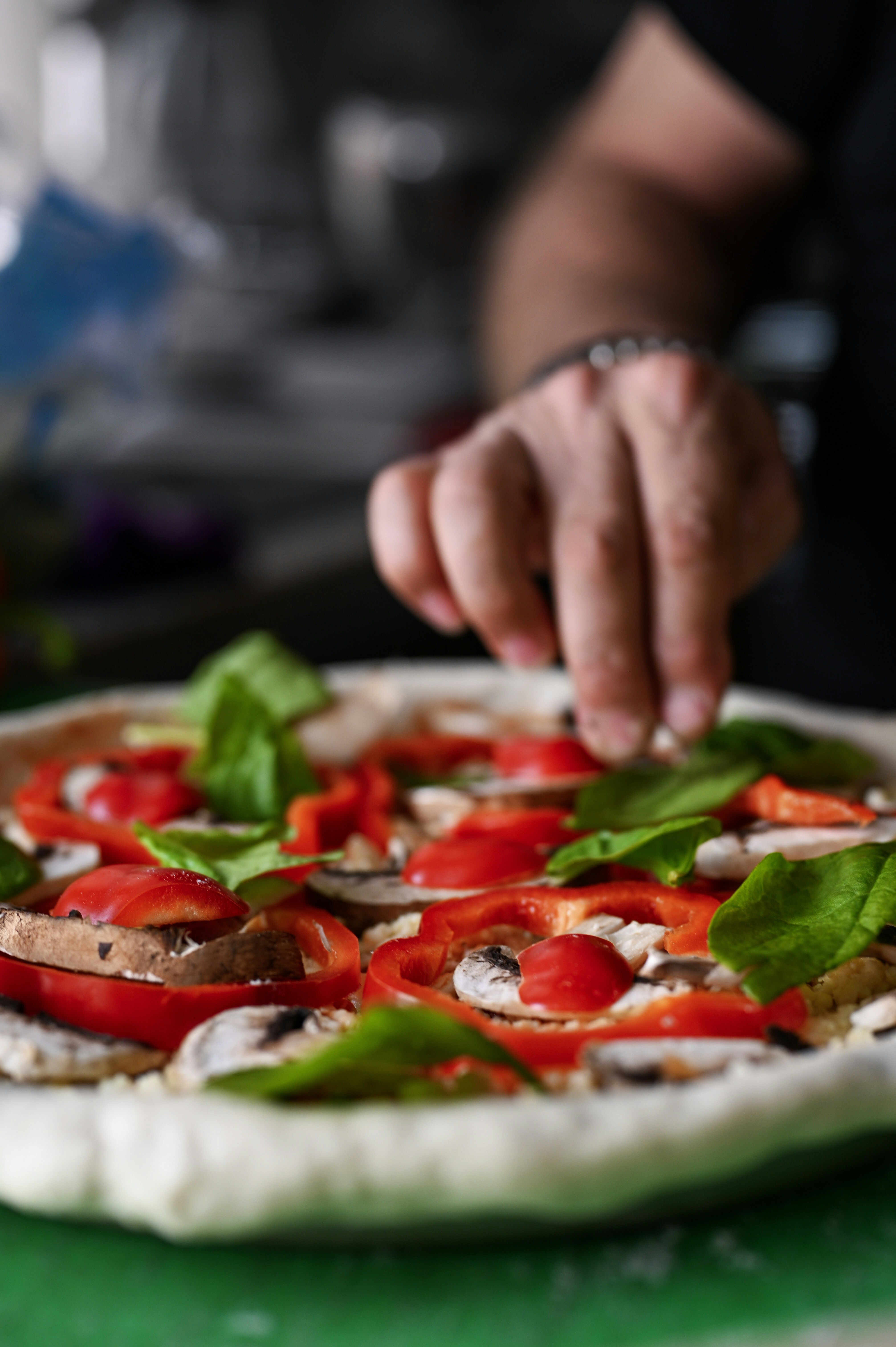 Mano che aggiunge foglie di spinaci freschi su una pizza vegetariana cruda.