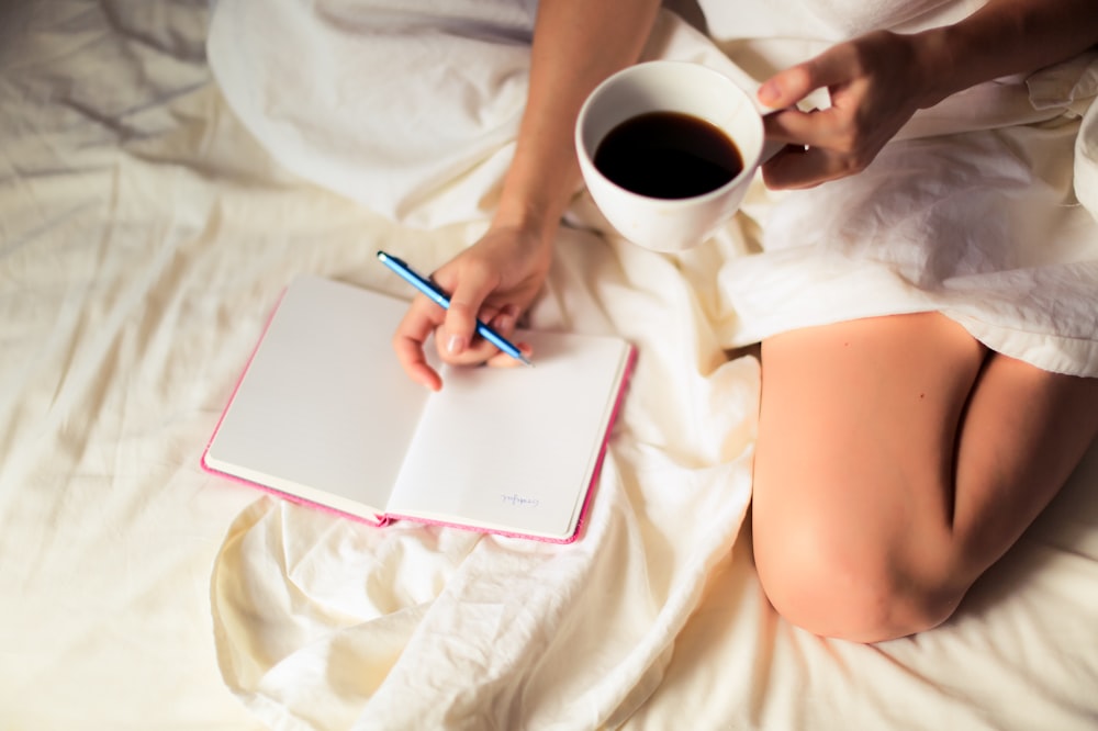 woman holding coffee cup while writing