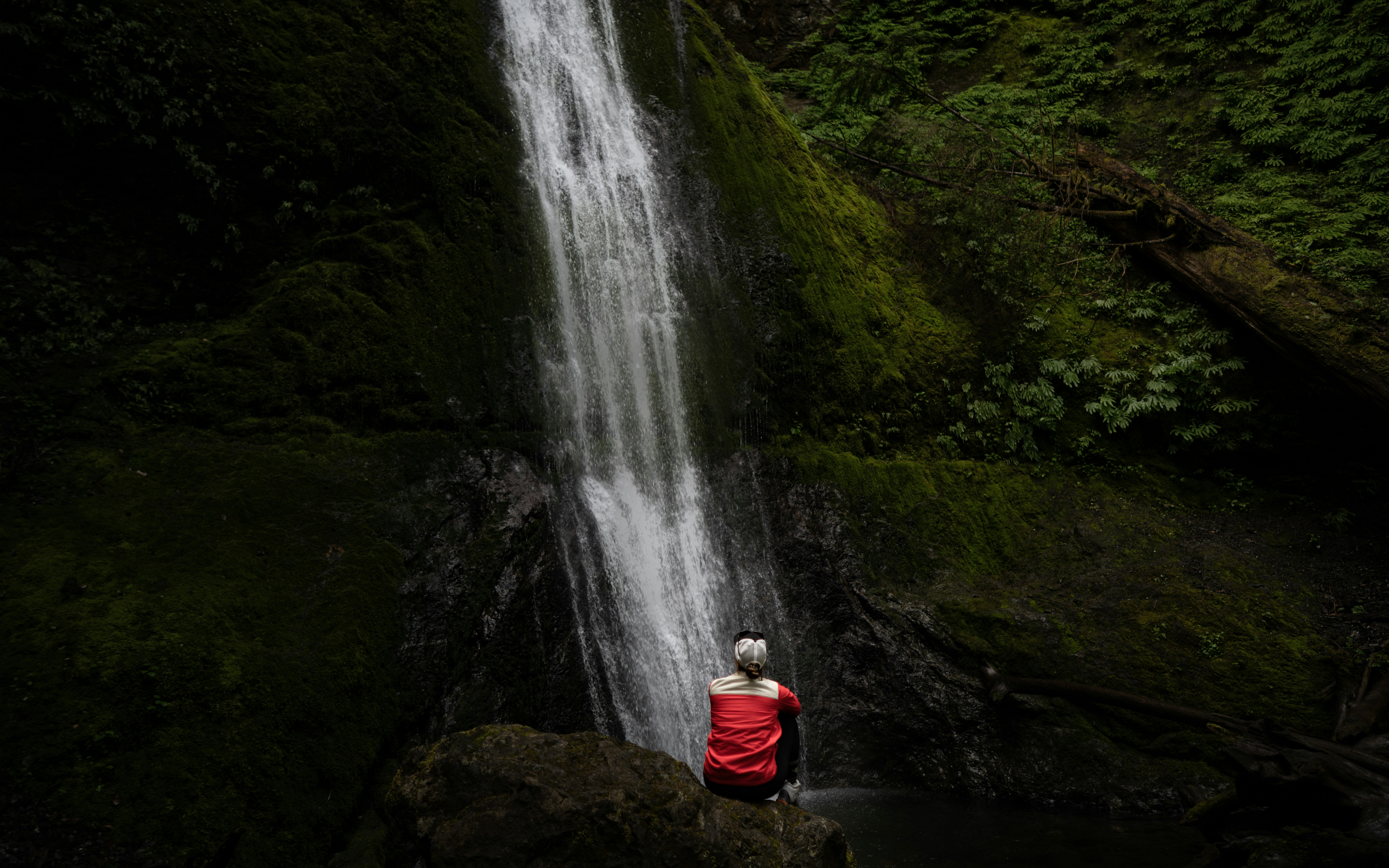 photography of person sitting on stone while facing on mountain during daytime