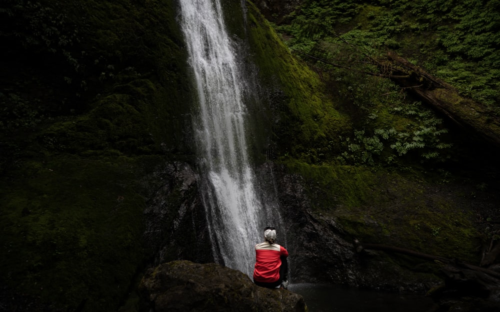 photography of person sitting on stone while facing on mountain during daytime