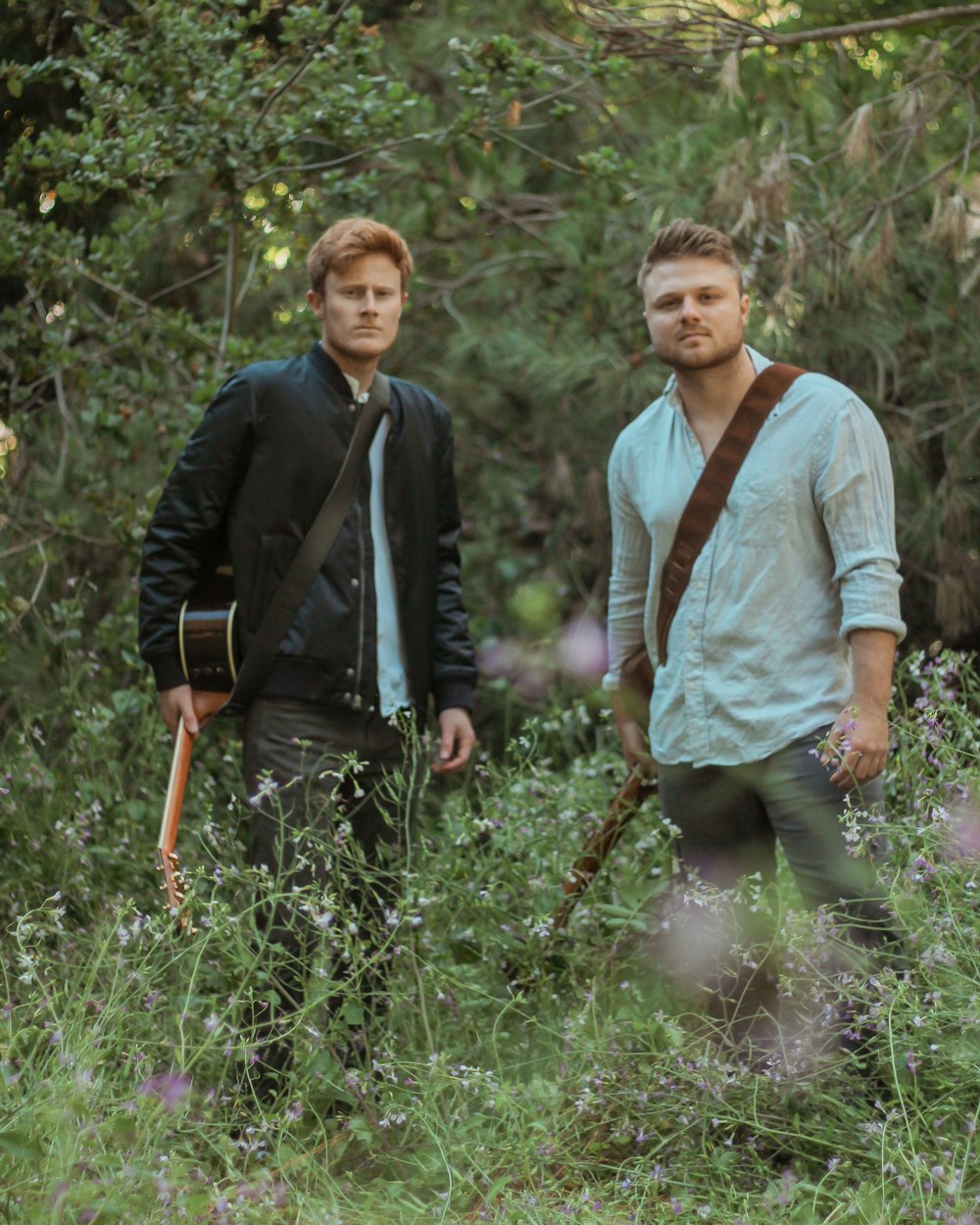 two men with guitars standing in forest