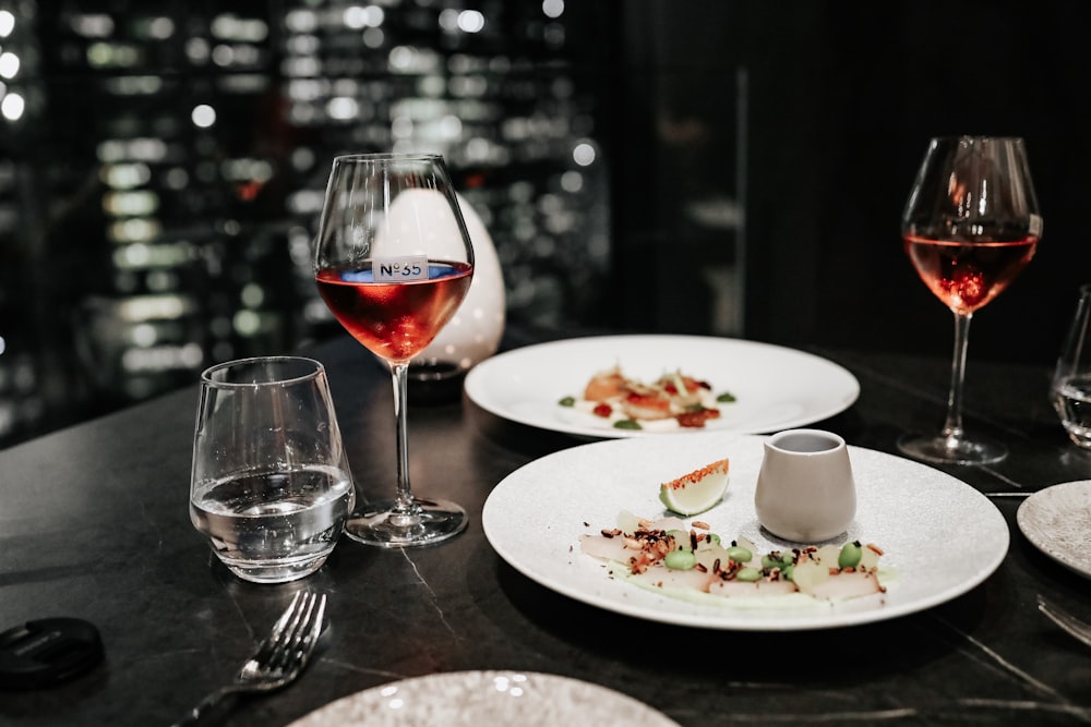 four clear glass wine cup near two white plate close-up photography