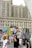 A large building serves as a backdrop for a vibrant, colorful mural featuring pop art elements, including bold patterns and stylized graphics of a face with red lips. People walk along the street in front of the mural, some appearing to be tourists capturing the scene. The mural and the urban surroundings create a lively atmosphere.