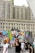 A large building serves as a backdrop for a vibrant, colorful mural featuring pop art elements, including bold patterns and stylized graphics of a face with red lips. People walk along the street in front of the mural, some appearing to be tourists capturing the scene. The mural and the urban surroundings create a lively atmosphere.