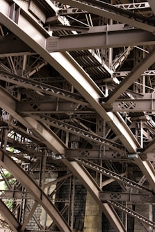 Intricate metal beams and structures form an elaborate framework, showcasing industrial design and engineering. The complex web of girders features rivets and cross-bracing against a backdrop of masonry.