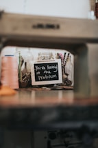 A small chalkboard sign with the words 'You're looking at the problem' is placed amongst jars containing various items like pencils and coins. The jars and sign are located on a wooden surface, with some sewing supplies like a spool of thread visible.