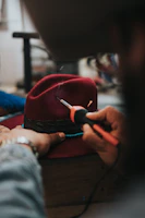 An artisan carefully stitching a custom logo onto a black ballcap in a cozy workshop setting.