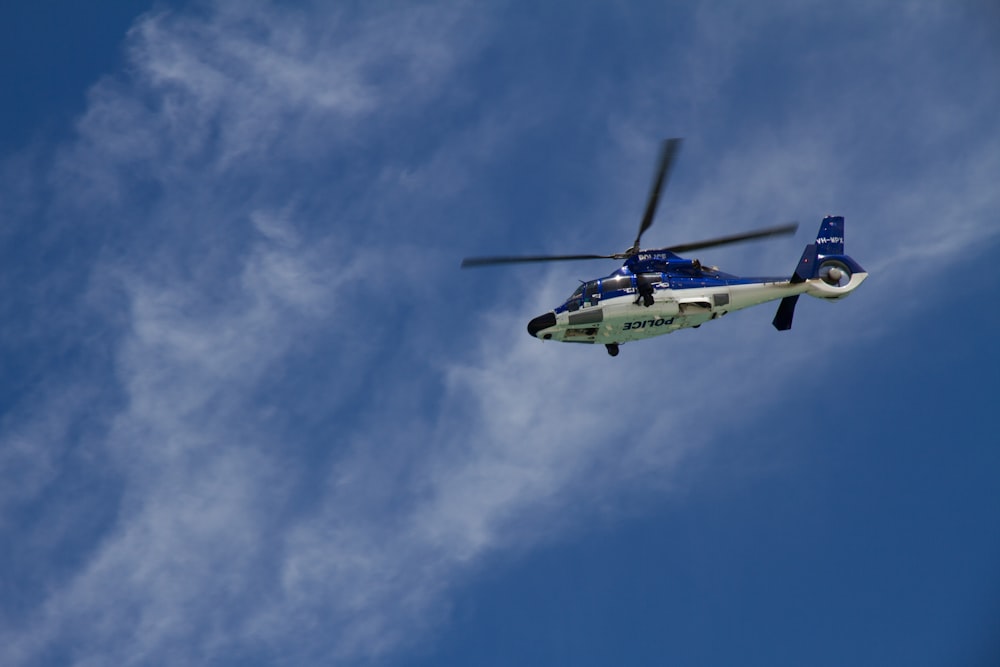 low-angle photography of white and blue helicopter under blue sky