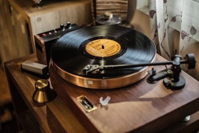 A vintage wooden turntable with a vinyl record spinning on it, set in a warm and cozy atmosphere. The record's label is clearly visible, and the tonearm is positioned over the grooves. Nearby objects include a small amplifier and various electronic components.