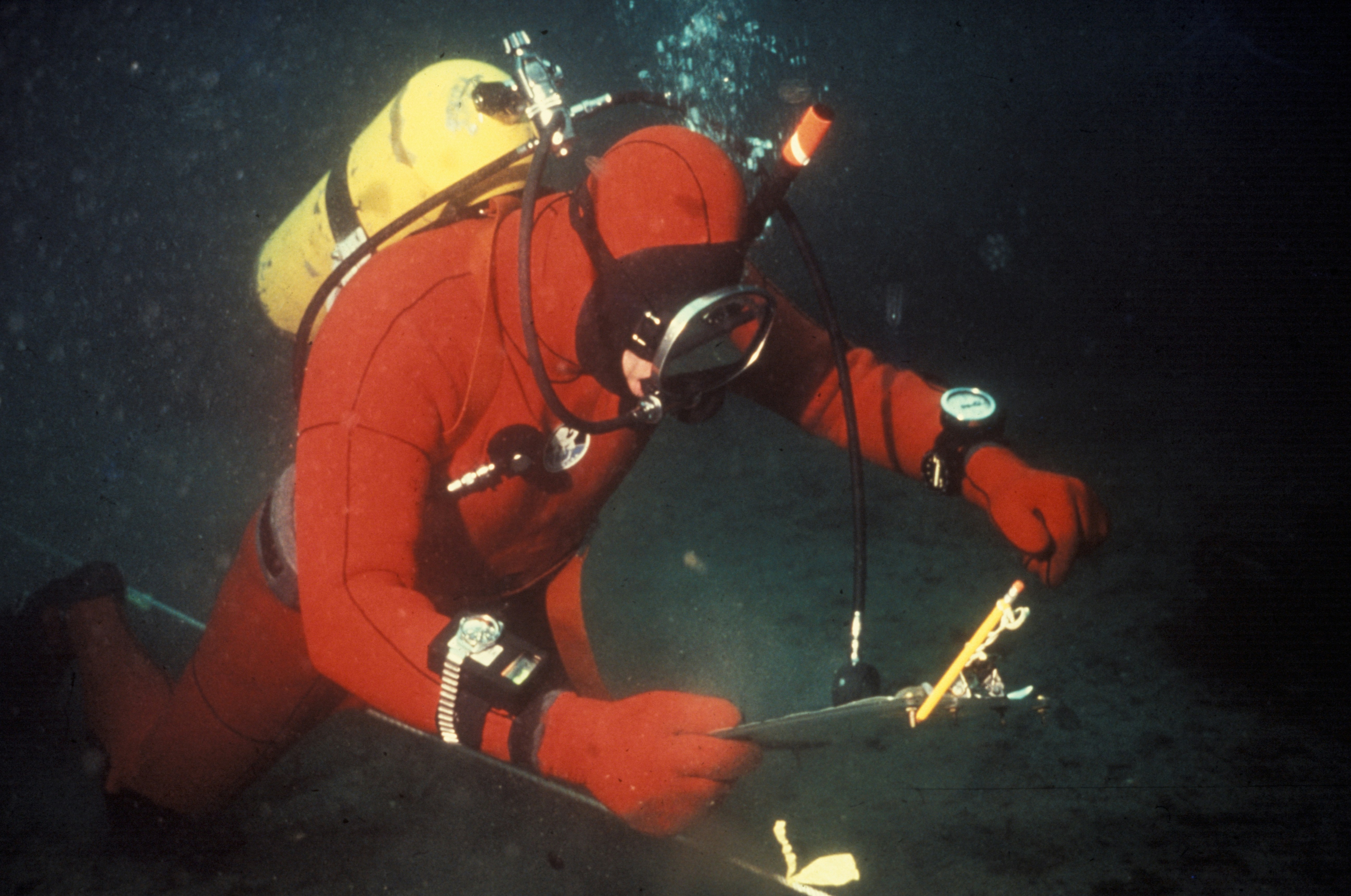 Diver in red diving suit checking a clipboard underwater