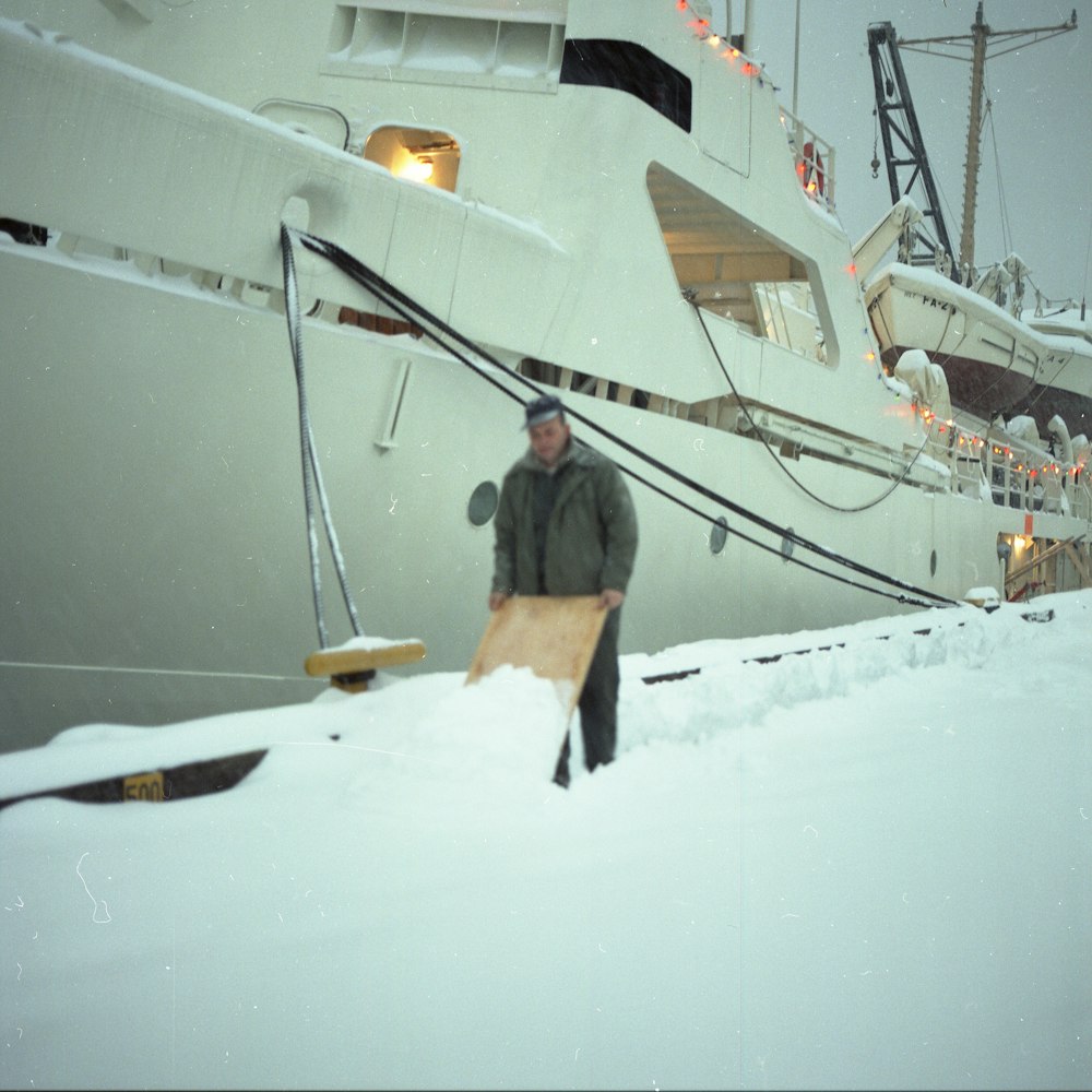 homme debout sur la neige près d’un bateau pendant la journée