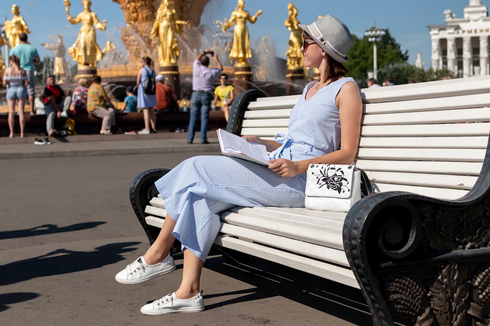 woman wearing blue sleeveless jumpsuit sitting on white and black wooden bench during daytime