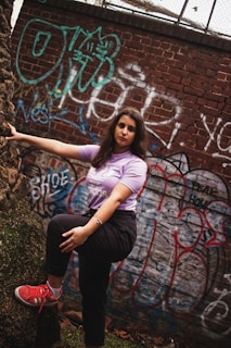 Model wearing a deep purple oversized tee standing against a gritty urban wall with graffiti