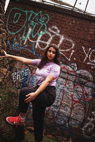 Model wearing a deep purple oversized tee standing against a gritty urban wall with graffiti