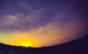 A vibrant sunset over a sacred mountain with deep purple and orange hues blending into the sky