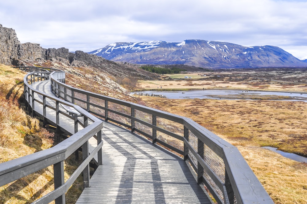 photography of gray wooden walkway near mountain during daytime