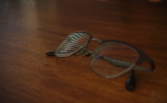 A close-up of stylish eyeglasses resting on a wooden table with a soft-focus background.