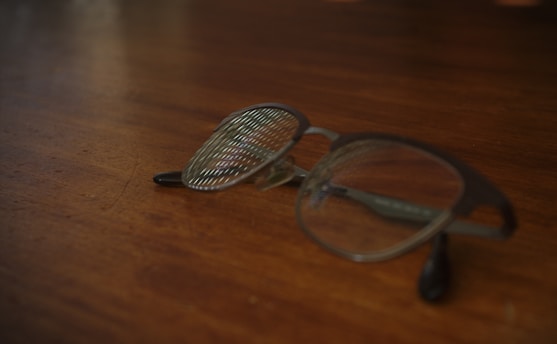 A close-up of stylish eyeglasses resting on a wooden table with a soft-focus background.