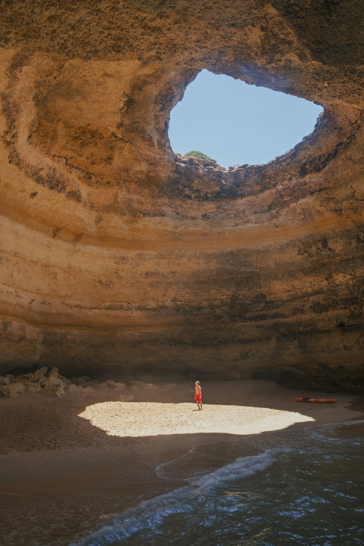 Person standing inside Benagil Cave with sunlight streaming through the natural skylight, Algarve Portugal