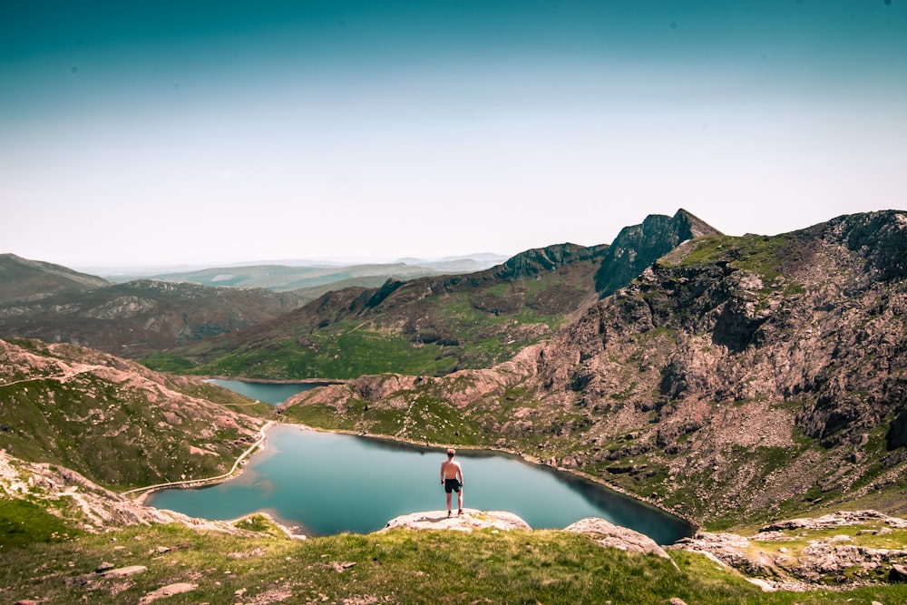 person standing on mountain beside lake during daytime
