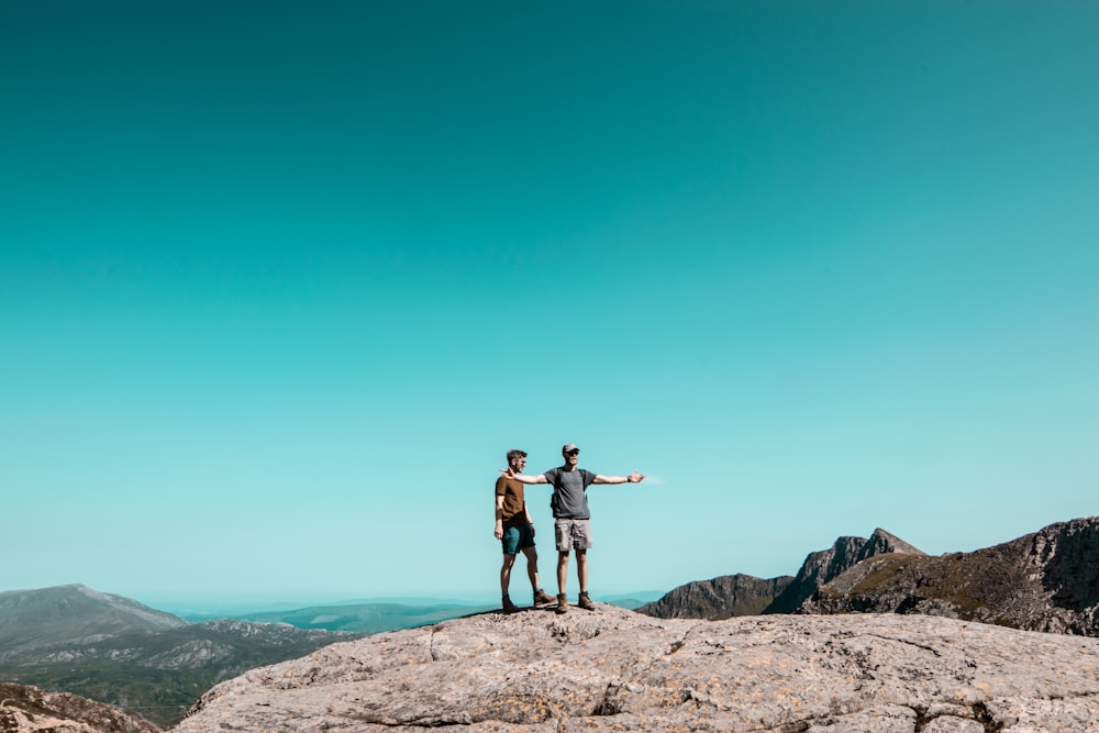 two men standing on top of grey rock hill