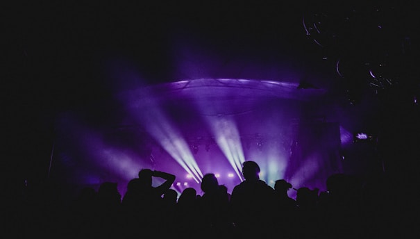 A vibrant concert scene with multicolored lights casting across a stage filled with people. Silhouettes of the audience are visible, creating a dynamic and lively atmosphere.