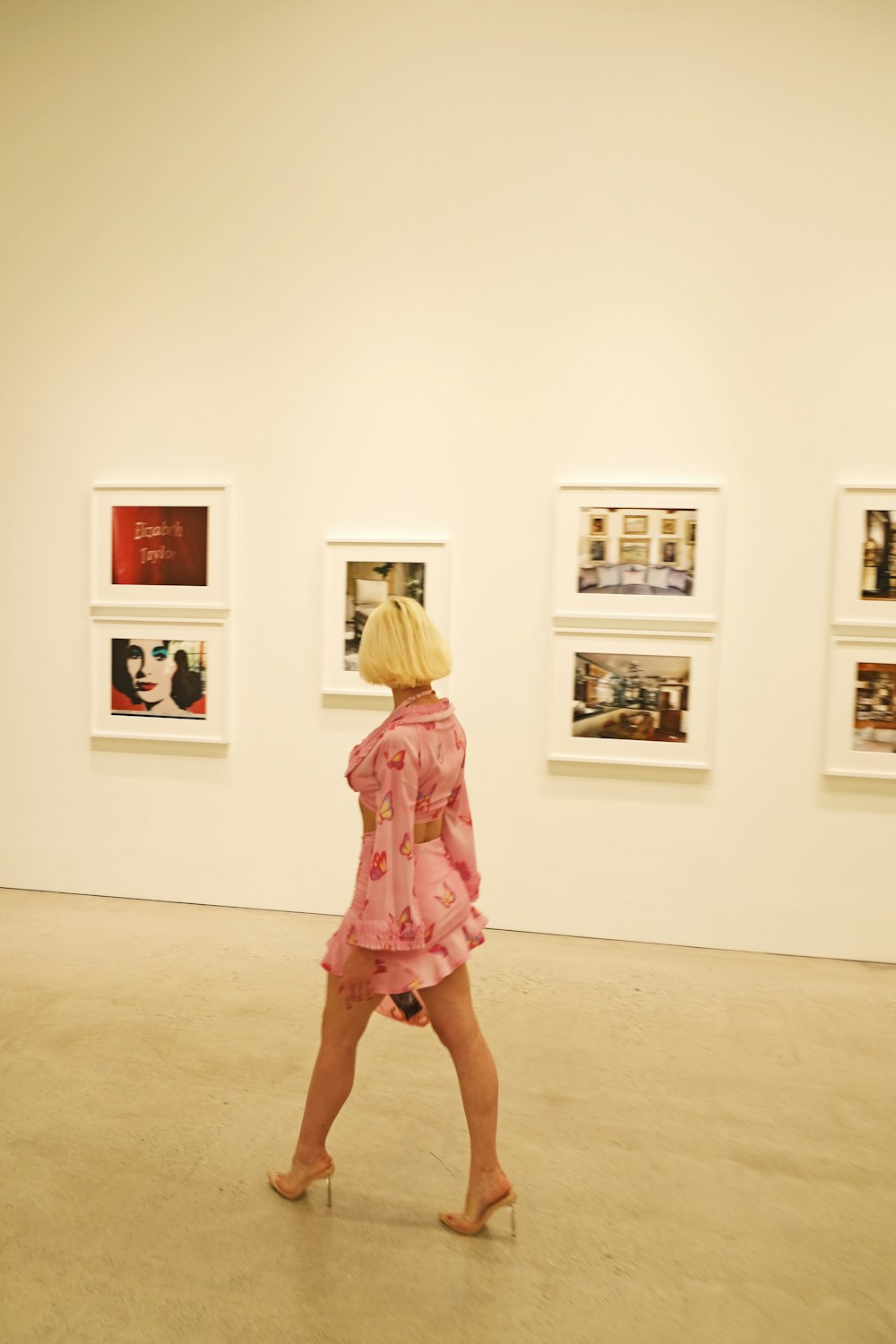 woman wearing pink floral long-sleeved dress walking besides paintings