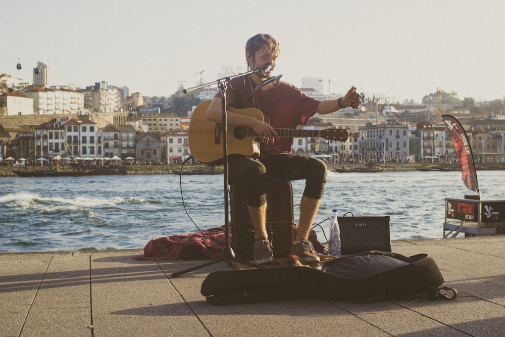 man wearing red shirt playing acoustic guitar on street during daytime