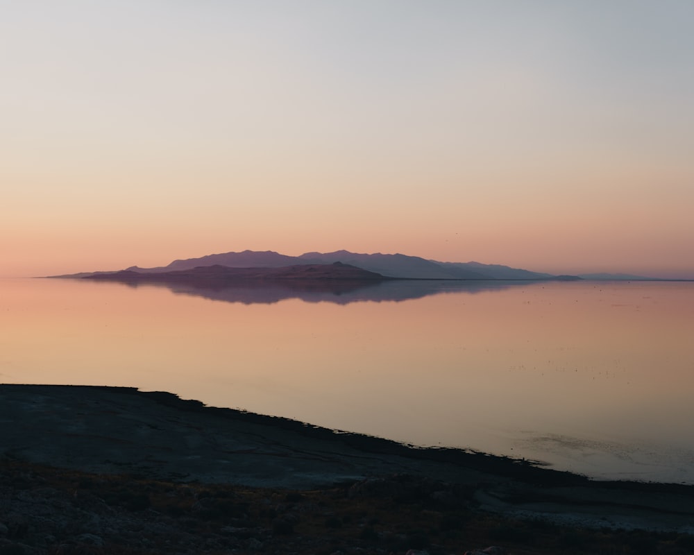 silhouette of island under orange sky at sunset