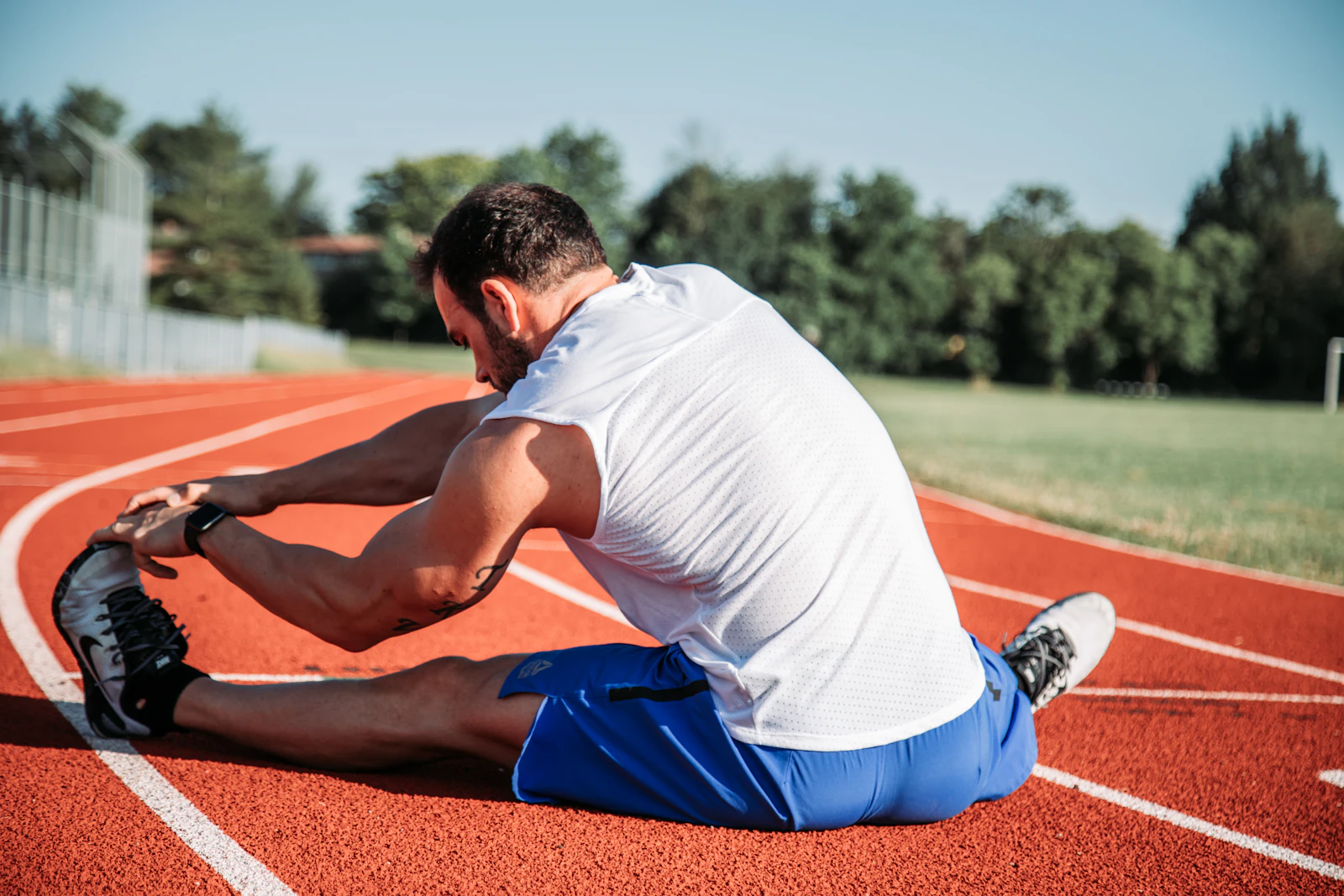 Athlete stretching his hamstrings on a red running track