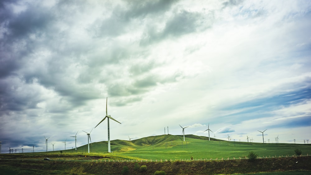 landscape photography of wind mills on green field under cloudy sky during daytime