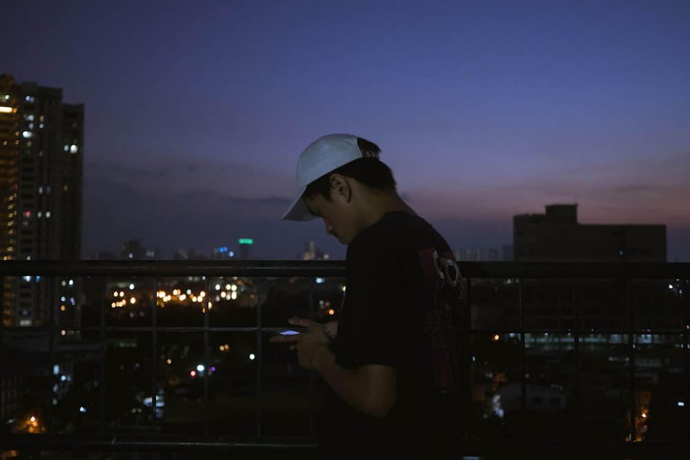 a man standing on a balcony at night looking at his cell phone