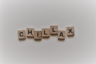 Wooden tiles spell out the word 'CHILLAX' on a plain, light background. Each tile contains a letter and a small number in the bottom right corner.