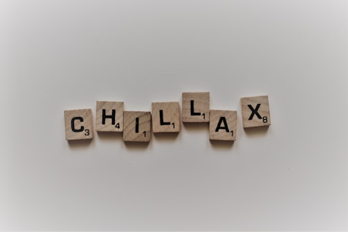 Wooden tiles spell out the word 'CHILLAX' on a plain, light background. Each tile contains a letter and a small number in the bottom right corner.