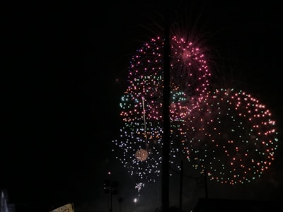 Bright and colorful fireworks illuminate the night sky with bursts of red, green, and pink lights. The explosions create intricate and symmetrical patterns that stand out against the dark background.