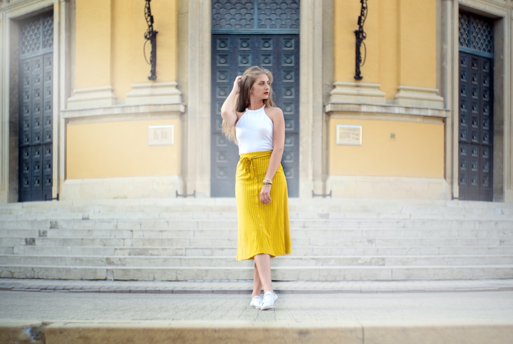 donna che indossa il vestito giallo e bianco che si leva in piedi accanto all'edificio durante il giorno