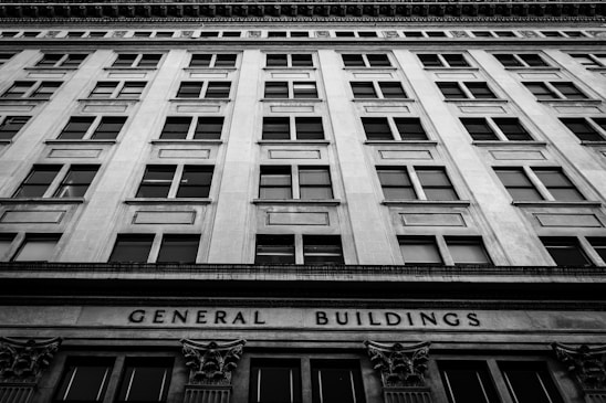 A black and white photograph of a tall, multi-story building with a symmetrical window arrangement. The facade features classical architectural elements and the words 'General Buildings' are prominently displayed at the base.