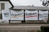 Large banners with bold text hang on the exterior wall of a building. The text is in German and translates to 'We women have rights!'. Several hashtags and the name 'UNIA' are visible on the right banner.