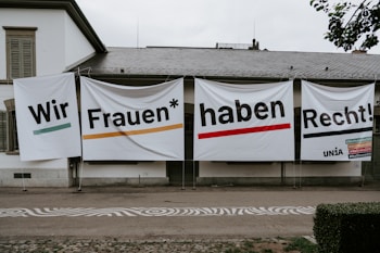 Large banners with bold text hang on the exterior wall of a building. The text is in German and translates to 'We women have rights!'. Several hashtags and the name 'UNIA' are visible on the right banner.