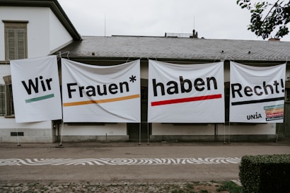 Large banners with bold text hang on the exterior wall of a building. The text is in German and translates to 'We women have rights!'. Several hashtags and the name 'UNIA' are visible on the right banner.